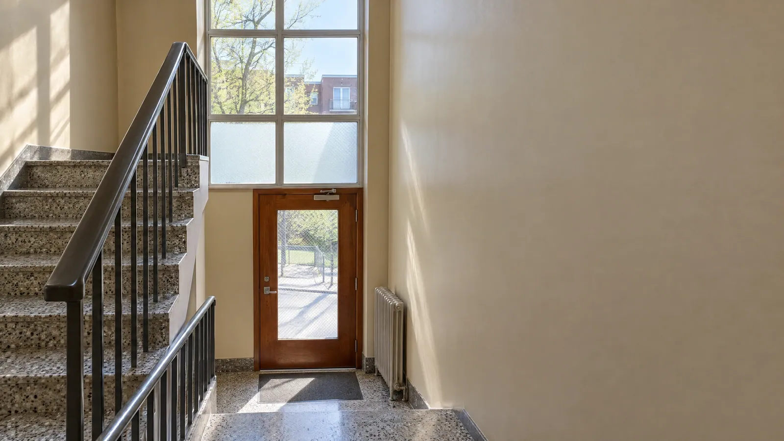 Stairwell of a small apartment building with a window on the landing and a glazed door opening onto the corridor