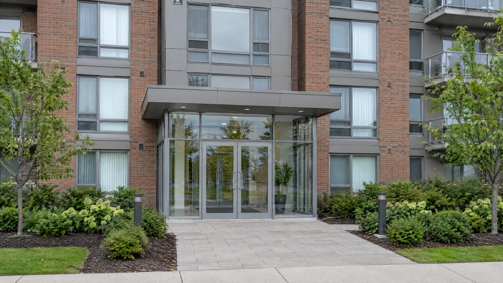 Condominium building entrance with a glass vestibule and a pair of aluminum doors, balconies with railings above