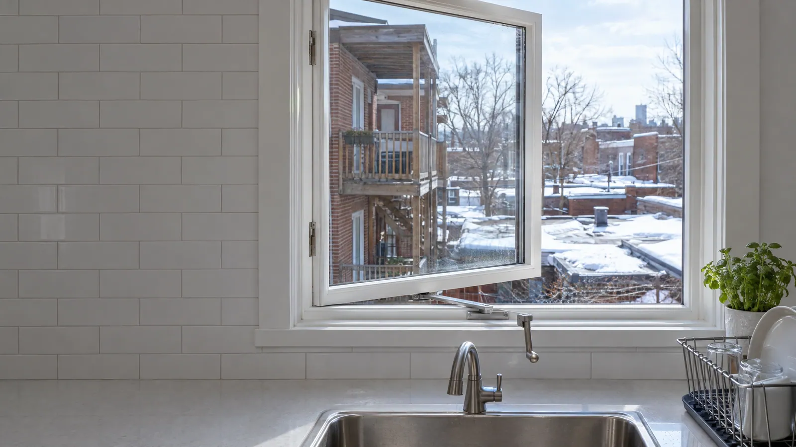 Plex kitchen casement window stuck partly open above the sink, with its crank handle and operator visible at the bottom of the frame