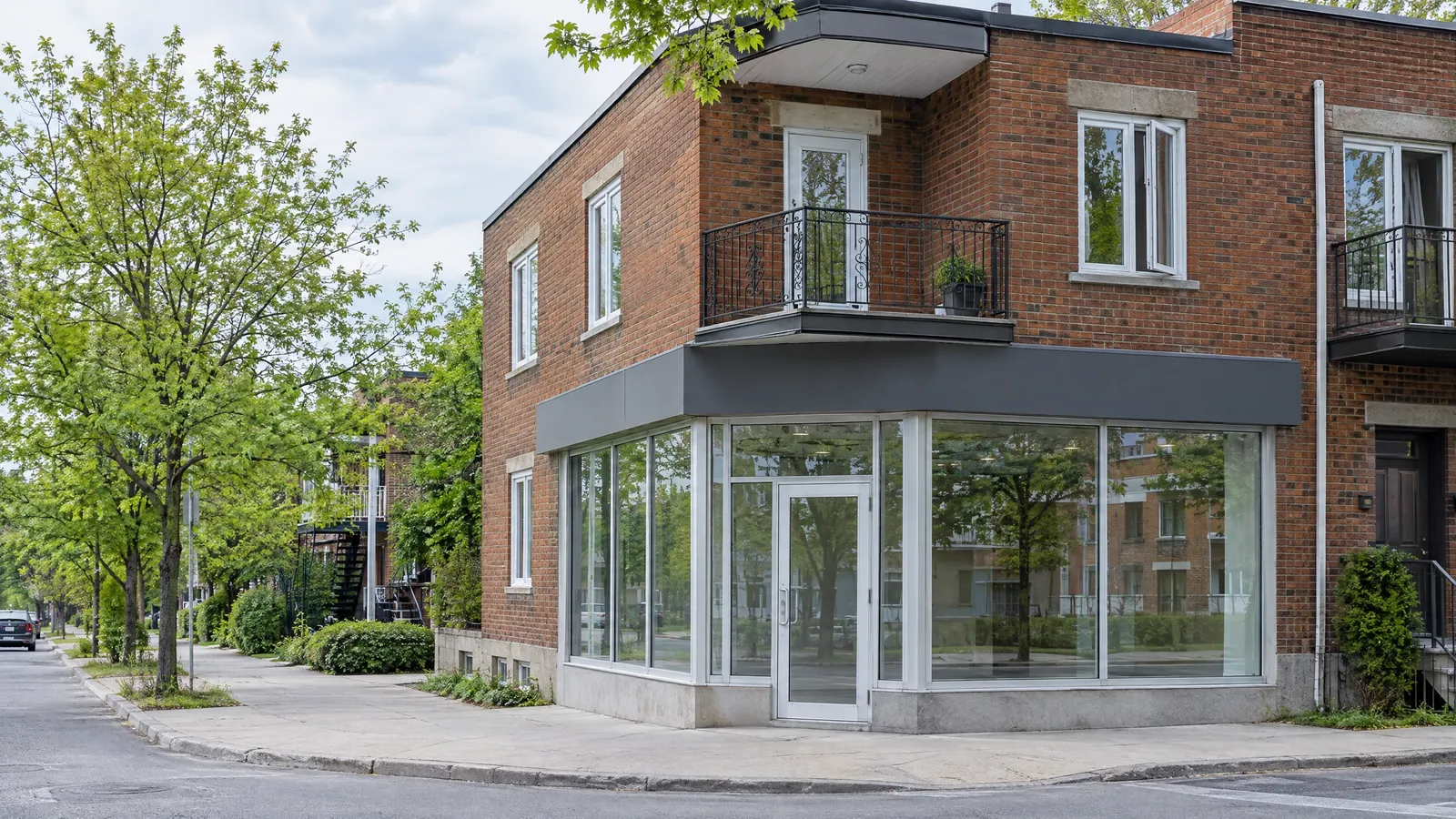 Brick corner building with a glass storefront at street level and plex flats with balconies above