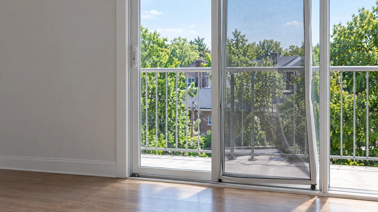 Sliding patio screen twisted and hanging off its bottom track, with an upper-floor balcony railing and treetops beyond
