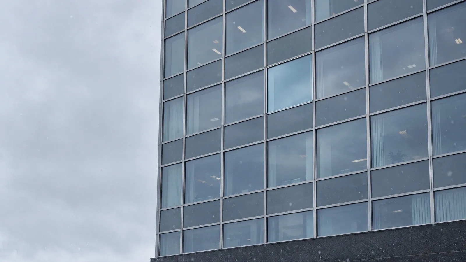 Glass curtain wall on an office building under a grey winter sky, with one newly replaced unit standing out among the older panes